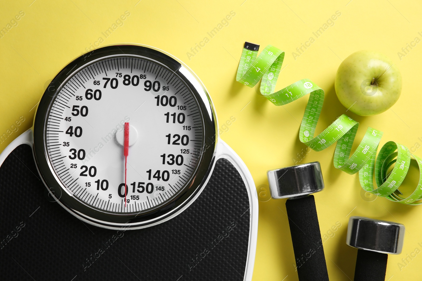 Photo of Bathroom scale, measuring tape, dumbbells and fresh apple on yellow background, flat lay