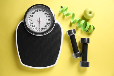 Photo of Bathroom scale, measuring tape, dumbbells and fresh apple on yellow background, flat lay