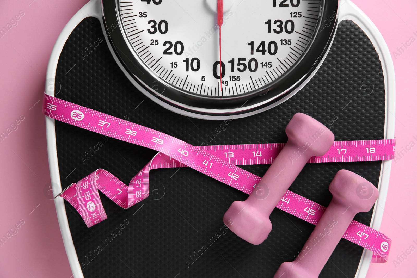 Photo of Scale tied with measuring tape and dumbbells on pink background, top view