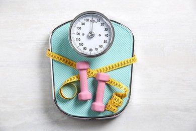 Photo of Bathroom scale, measuring tape and dumbbells on white wooden background, flat lay