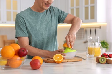 Photo of Man squeezing fresh orange with juicer at white marble table in kitchen, closeup