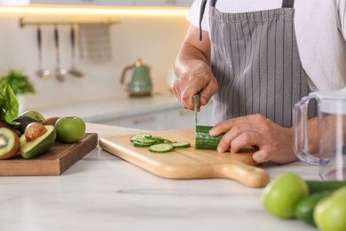 Man cutting fresh cucumber at white marble table, closeup