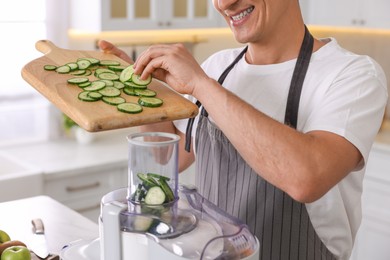 Photo of Man putting fresh cucumber into juicer at table in kitchen, closeup