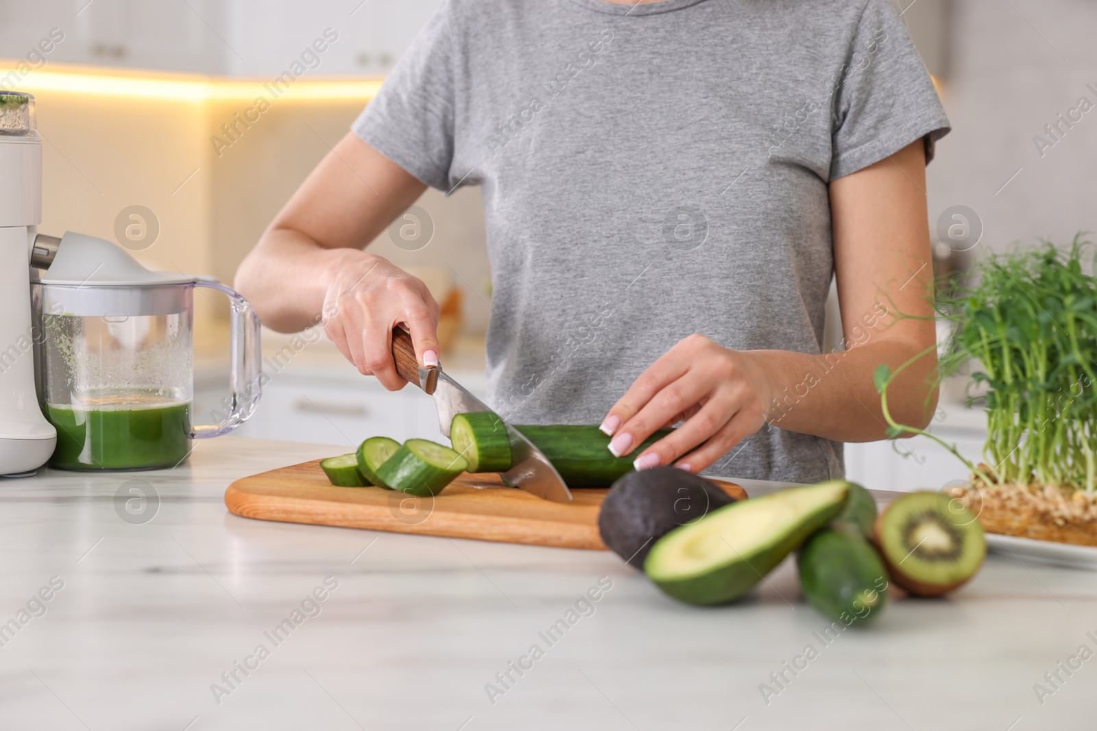 Photo of Woman cutting fresh cucumber at white marble table in kitchen, closeup