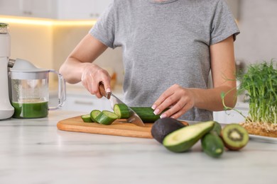 Woman cutting fresh cucumber at white marble table in kitchen, closeup