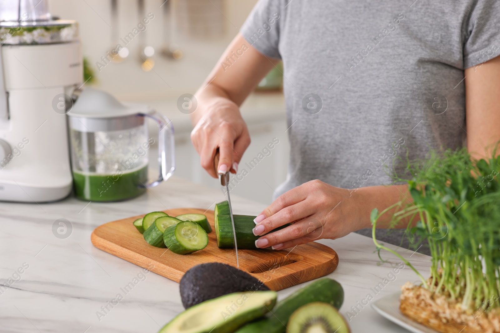 Photo of Woman cutting fresh cucumber at white marble table in kitchen, closeup