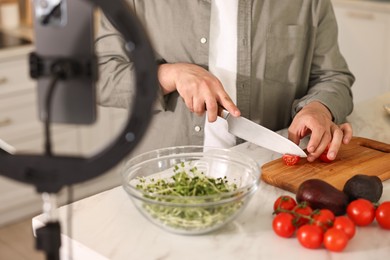 Photo of Food blogger cooking while recording video with smartphone and ring lamp in kitchen, closeup