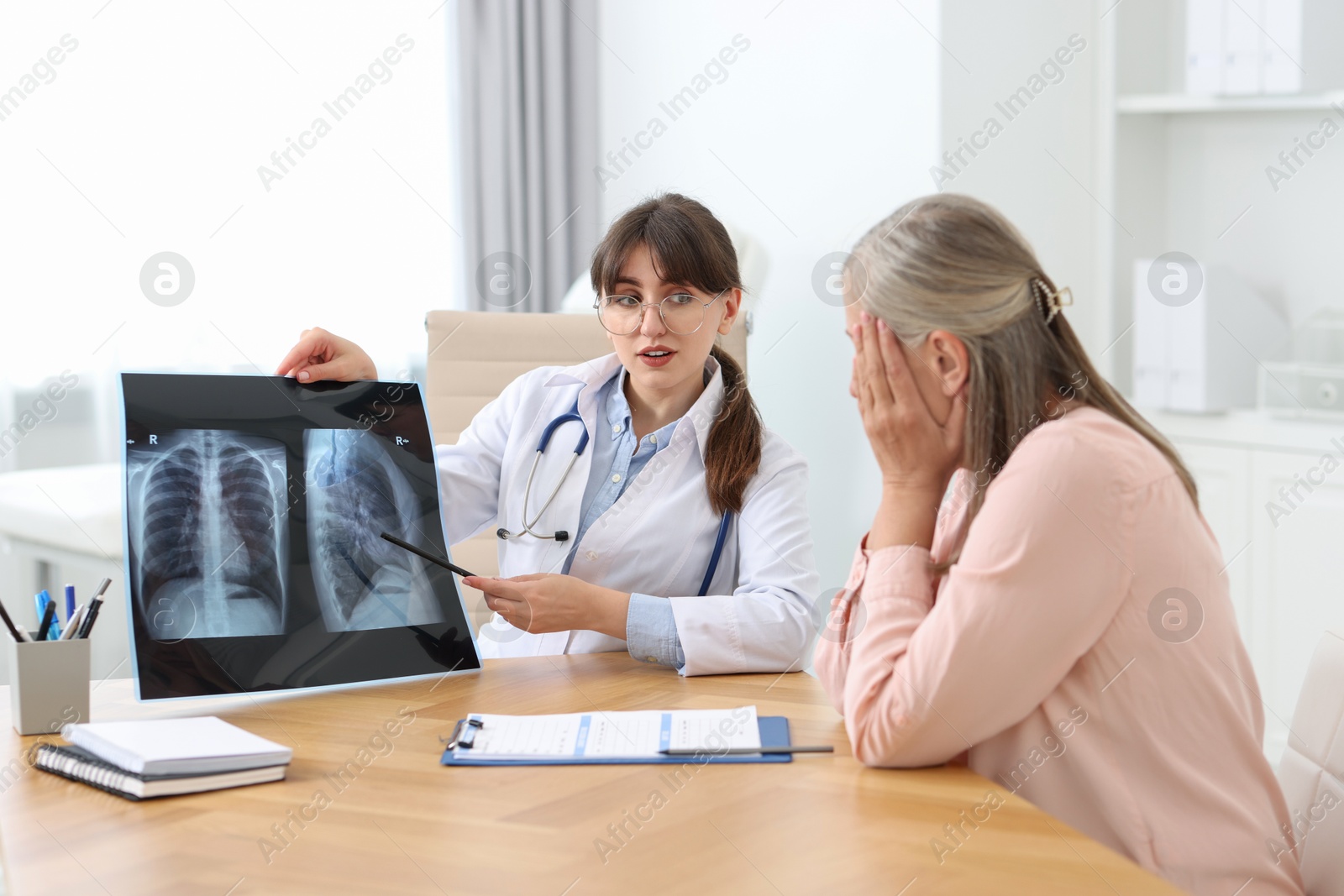 Photo of Lung disease. Doctor showing chest x-ray to her patient at table in clinic