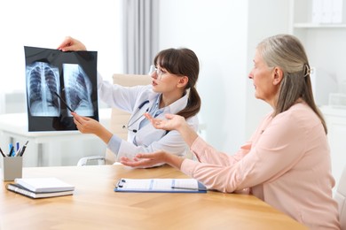 Photo of Lung disease. Doctor showing chest x-ray to her patient at table in clinic