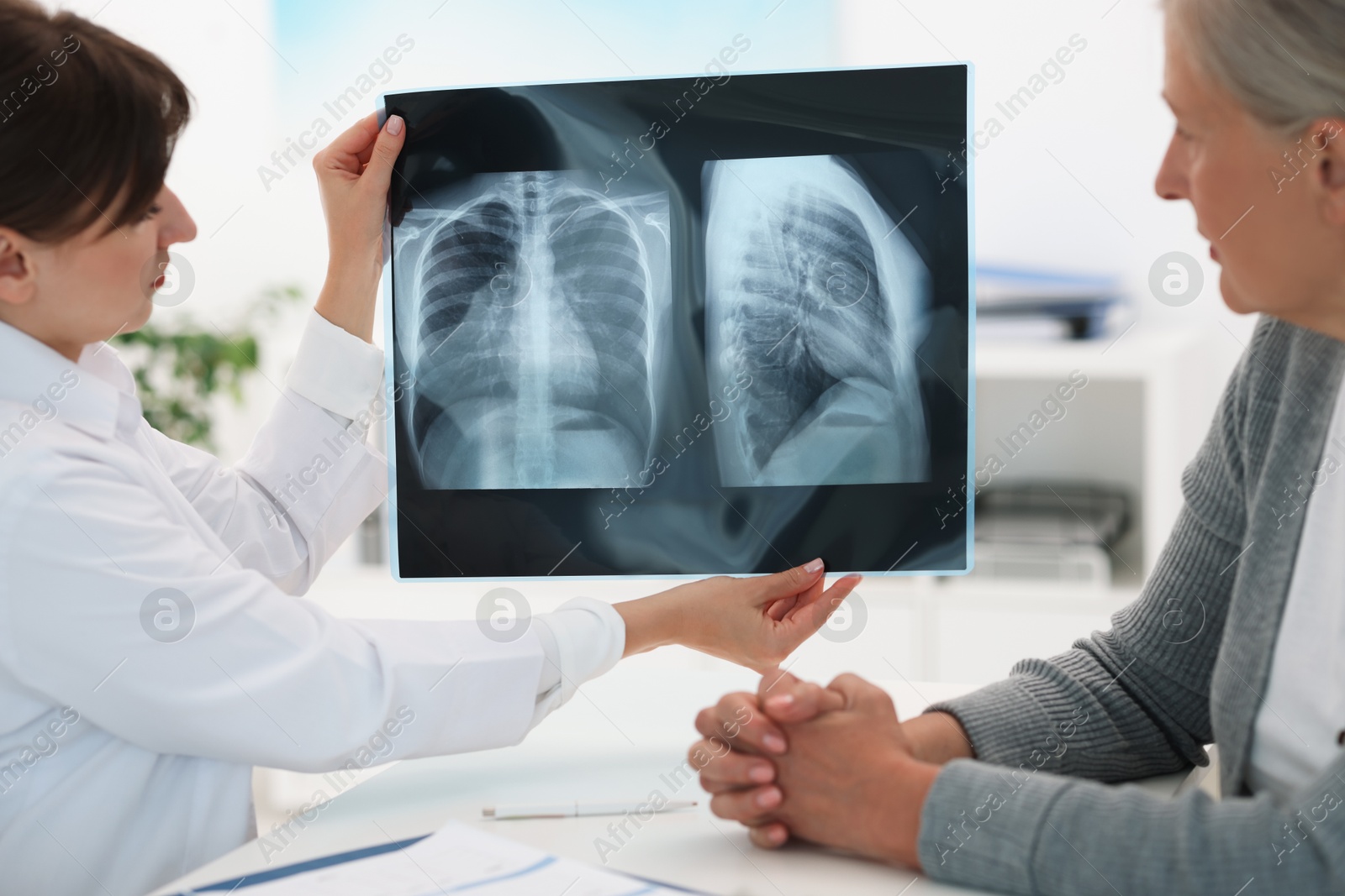 Photo of Lung disease. Doctor showing chest x-ray to her patient at table in clinic