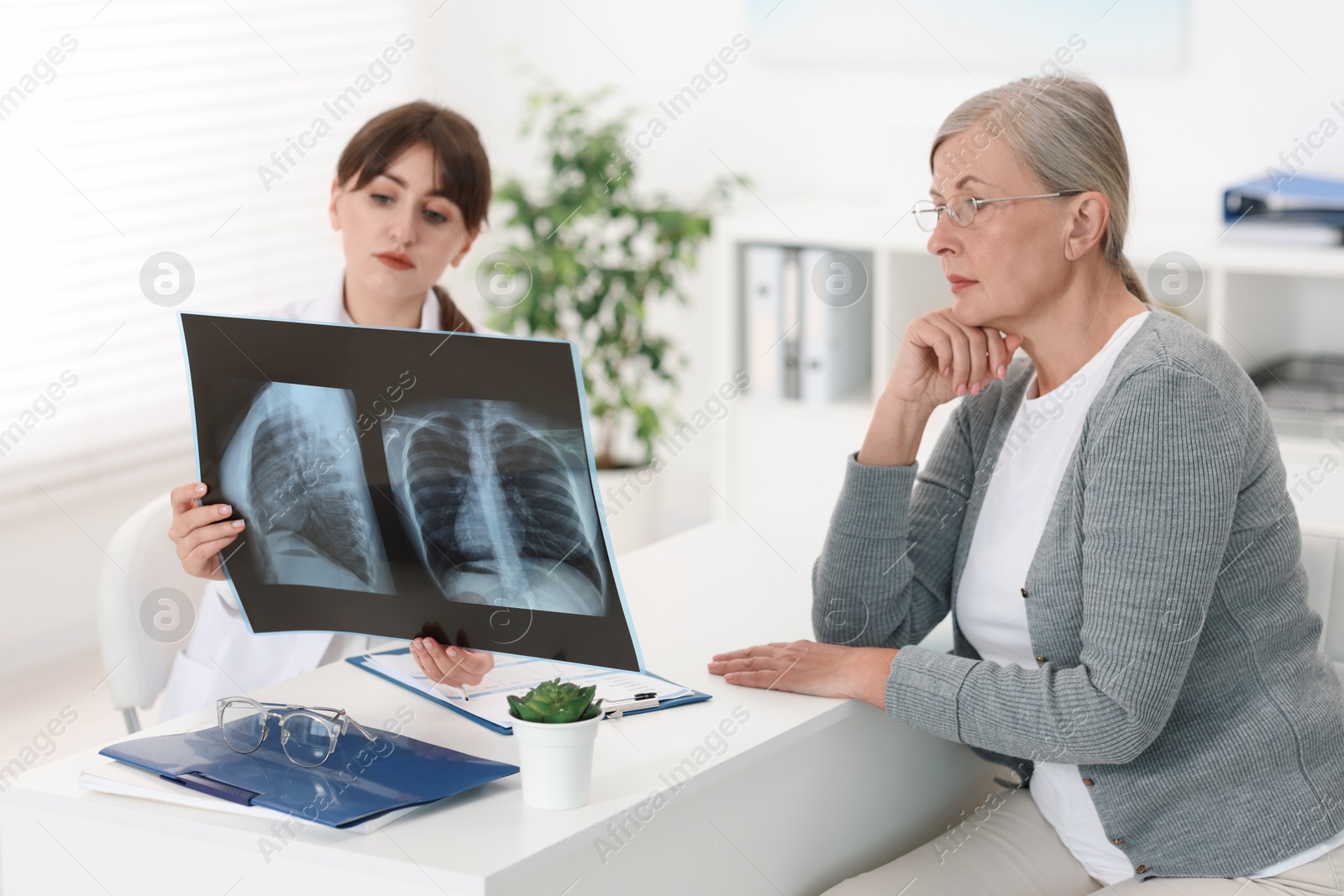 Photo of Lung disease. Doctor showing chest x-ray to her patient at table in clinic