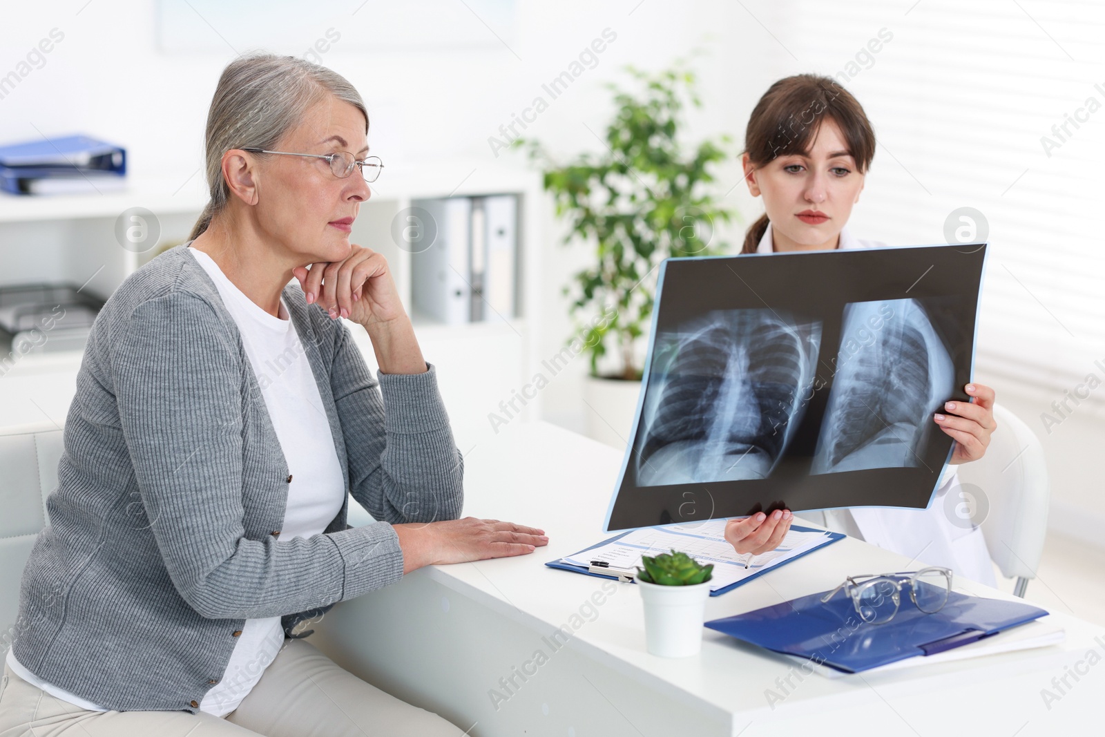 Photo of Lung disease. Doctor showing chest x-ray to her patient at table in clinic