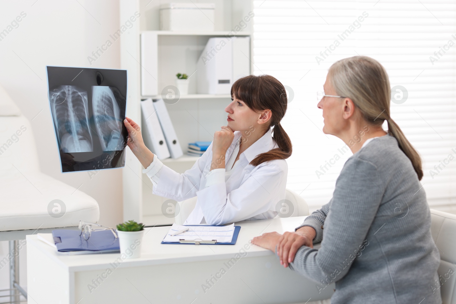 Photo of Lung disease. Doctor showing chest x-ray to her patient at table in clinic