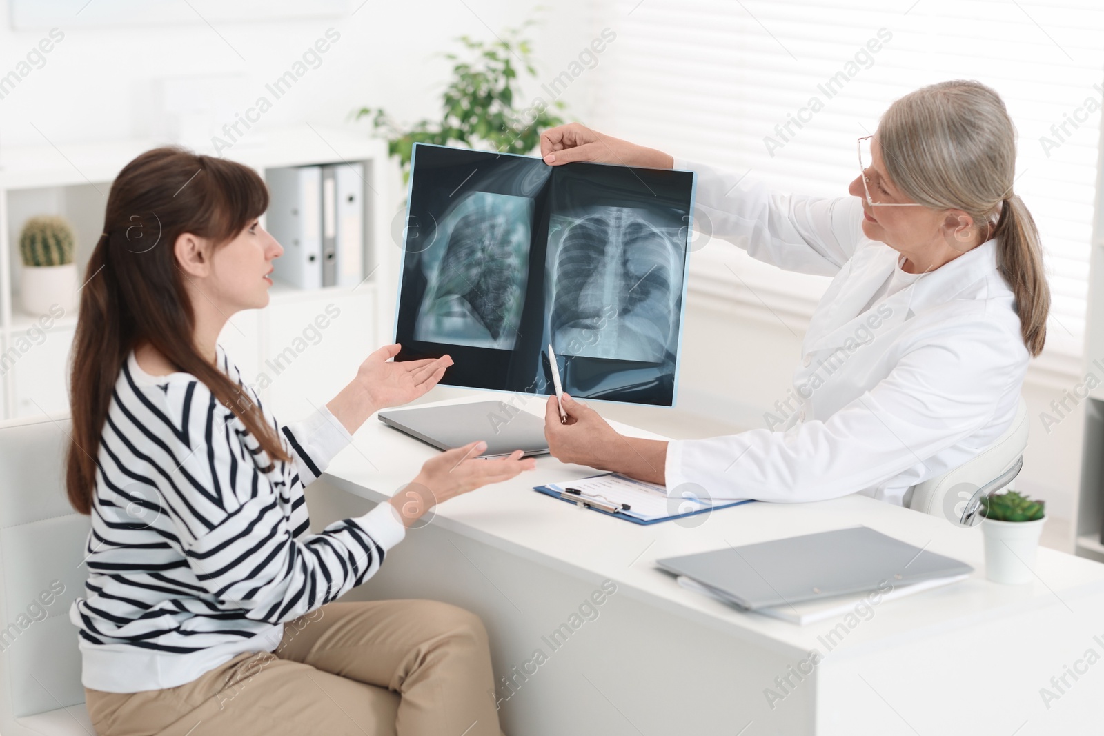 Photo of Lung disease. Doctor showing chest x-ray to her patient at table in clinic