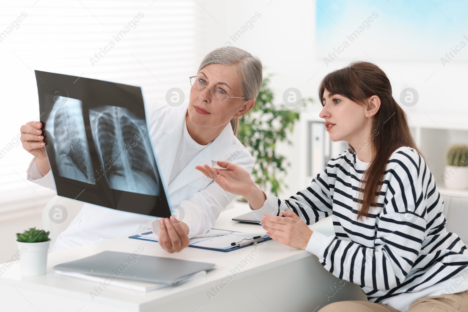 Photo of Lung disease. Doctor showing chest x-ray to her patient at table in clinic