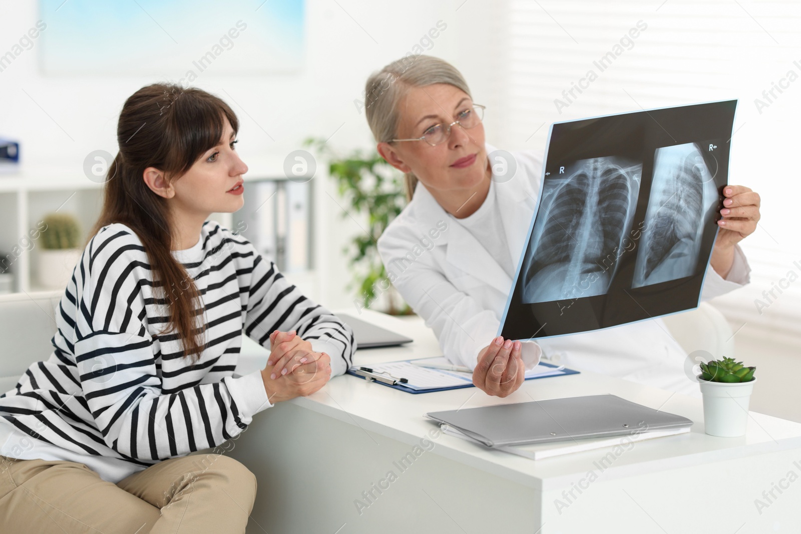 Photo of Lung disease. Doctor showing chest x-ray to her patient at table in clinic