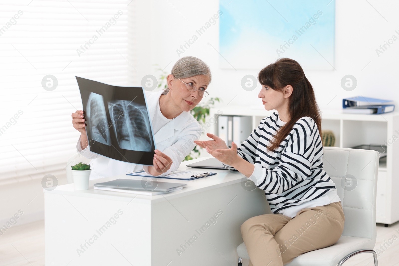 Photo of Lung disease. Doctor showing chest x-ray to her patient at table in clinic