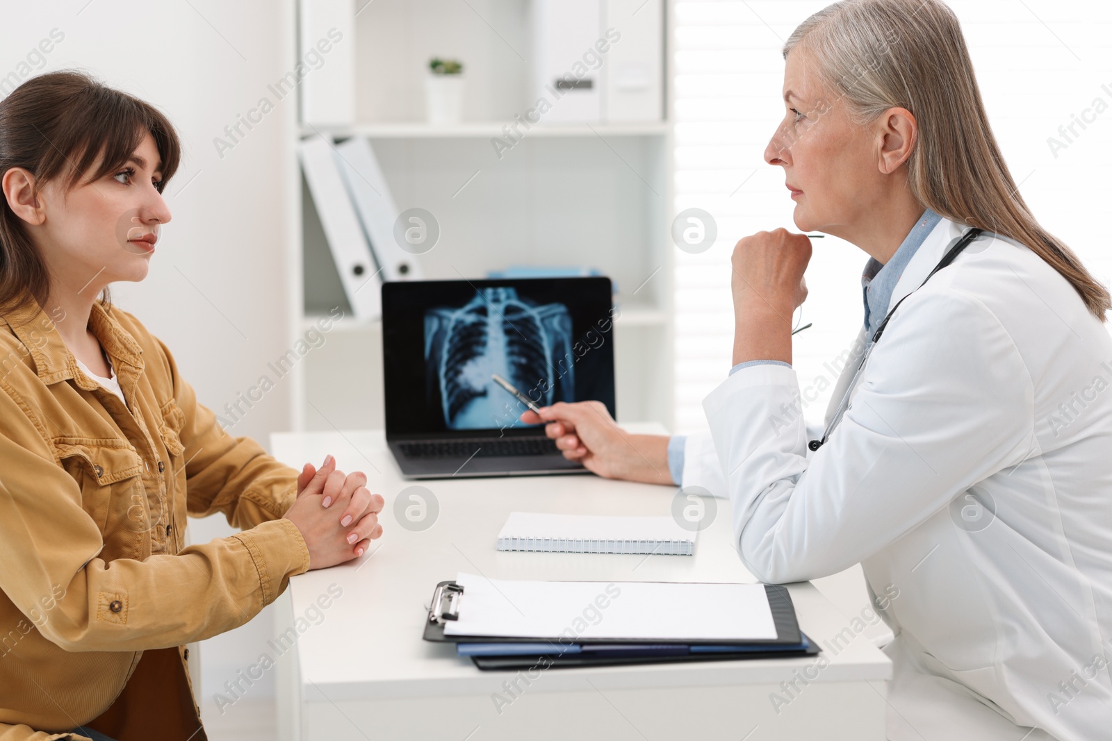 Photo of Lung cancer. Doctor showing chest x-ray on laptop to her patient in clinic