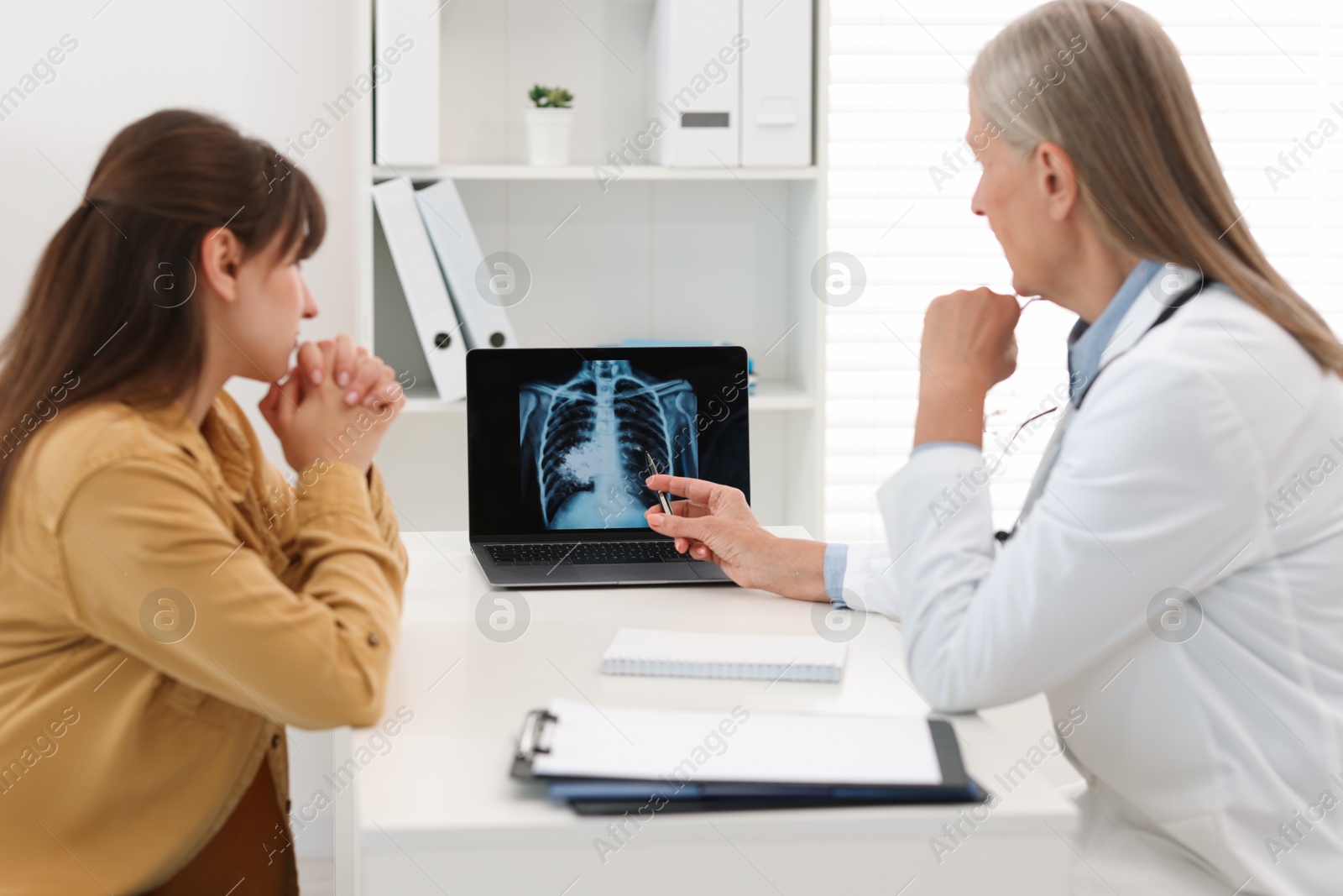 Photo of Lung cancer. Doctor showing chest x-ray on laptop to her patient in clinic