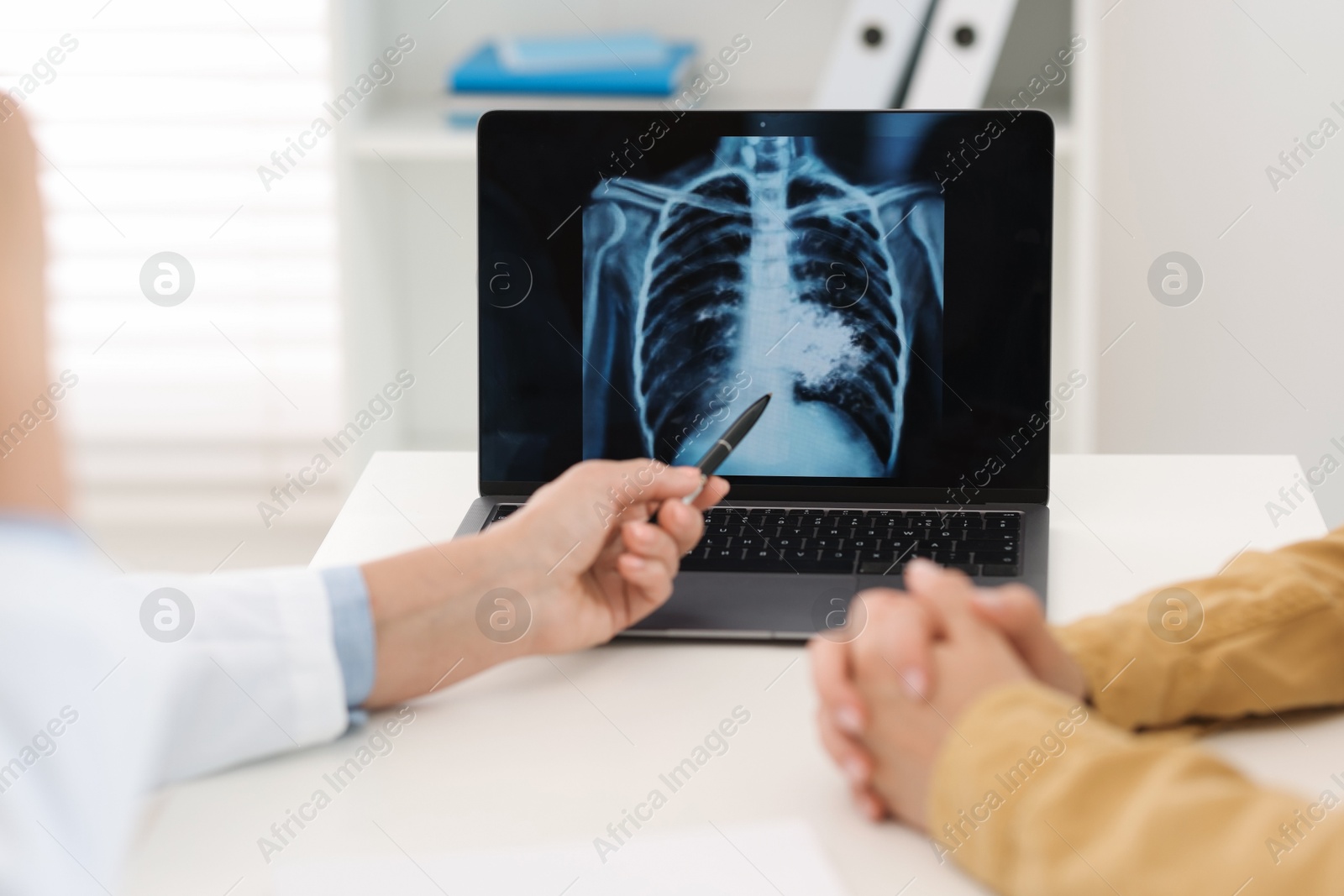 Photo of Lung cancer. Doctor showing chest x-ray on laptop to her patient in clinic, closeup