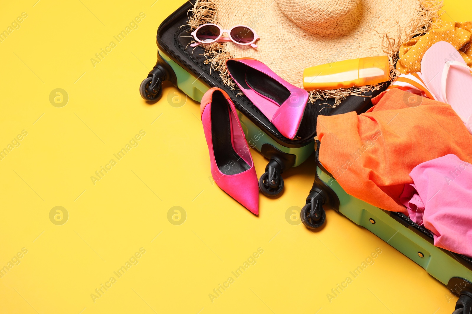 Photo of Open suitcase with traveler's belongings on yellow background, top view. Space for text