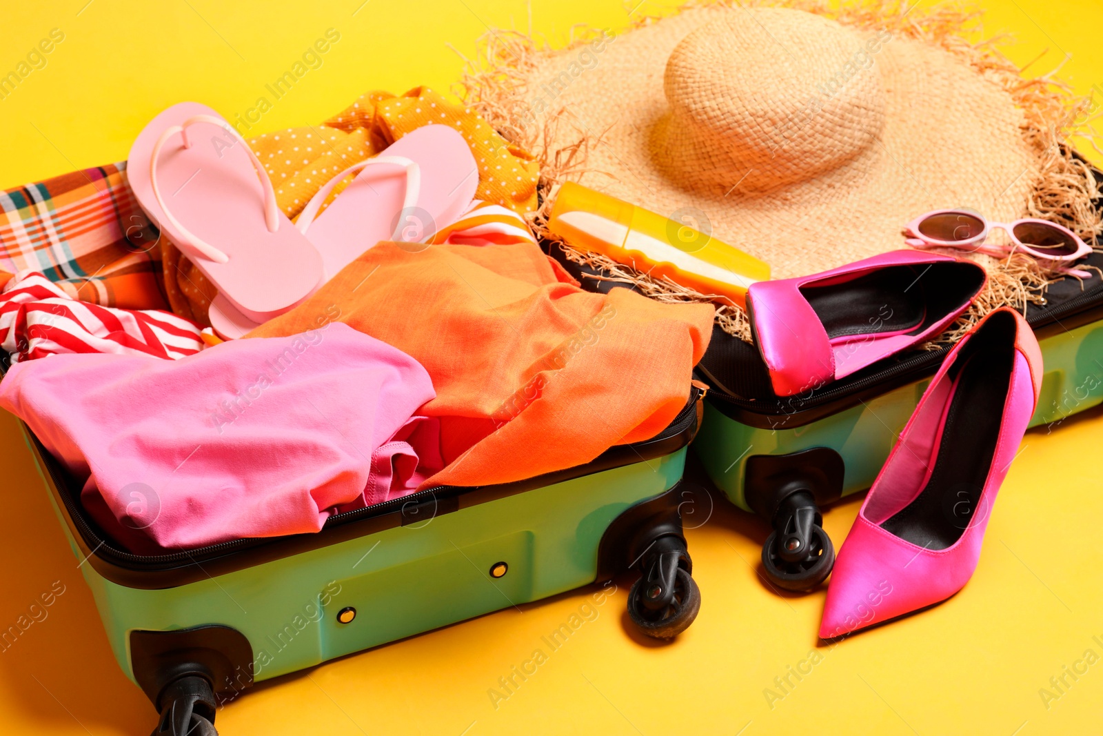 Photo of Open suitcase with traveler's belongings on yellow background, closeup