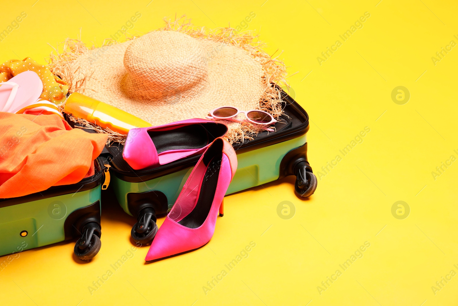 Photo of Open suitcase with traveler's belongings on yellow background, space for text