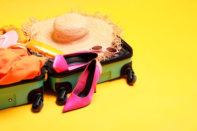 Photo of Open suitcase with traveler's belongings on yellow background, space for text