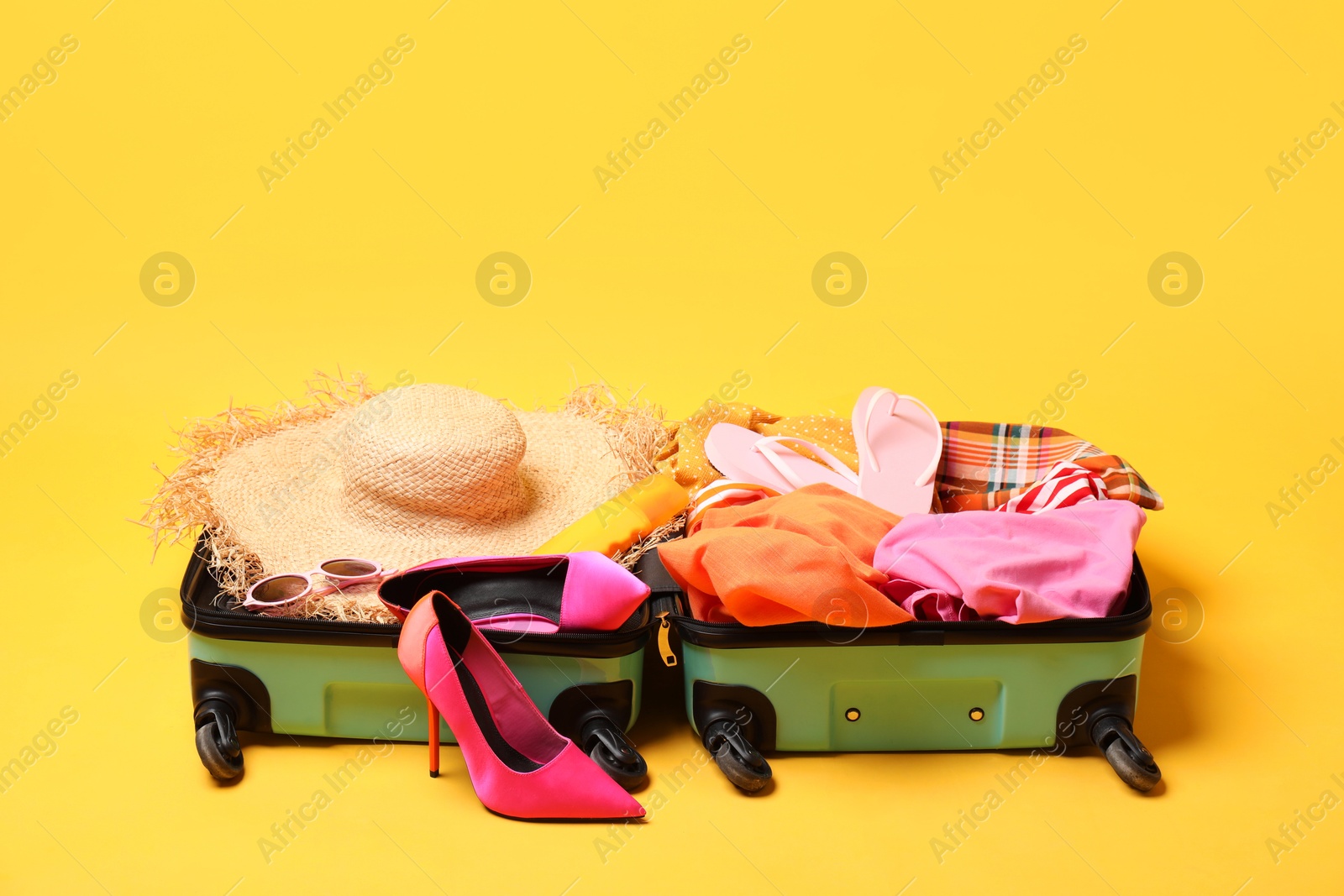 Photo of Open suitcase with traveler's belongings on yellow background