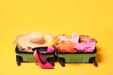 Open suitcase with traveler's belongings on yellow background