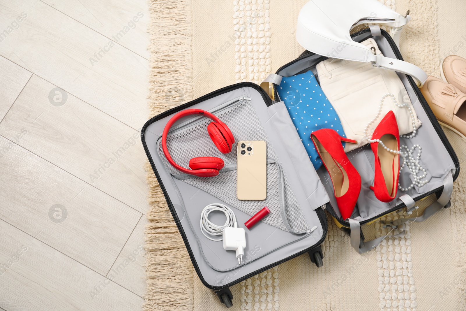 Photo of Open suitcase with traveler's belongings on floor, top view. Space for text