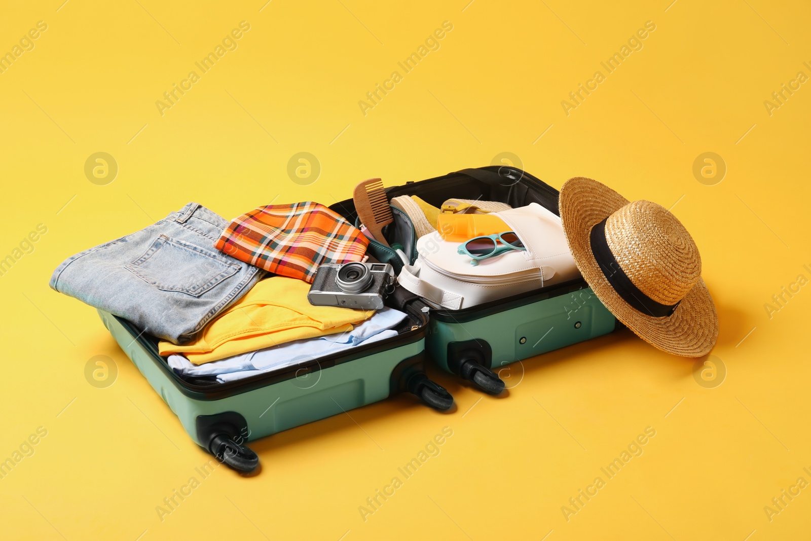 Photo of Open suitcase with traveler's belongings on yellow background