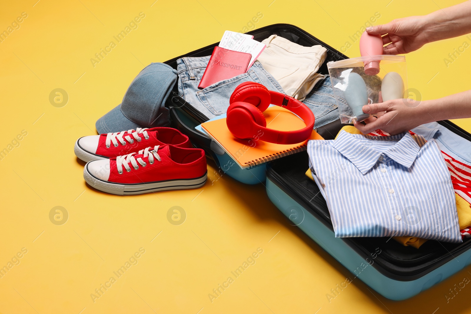 Photo of Woman packing suitcase for trip on yellow background, closeup