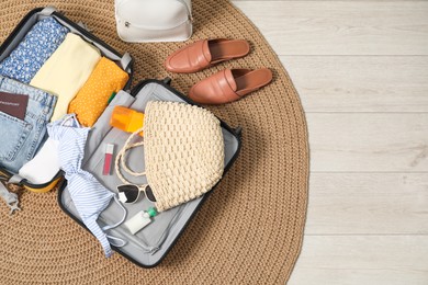 Open suitcase with traveler's belongings on rug, flat lay. Space for text