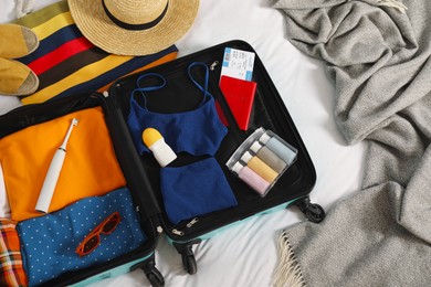 Open suitcase with traveler's belongings on bed, flat lay