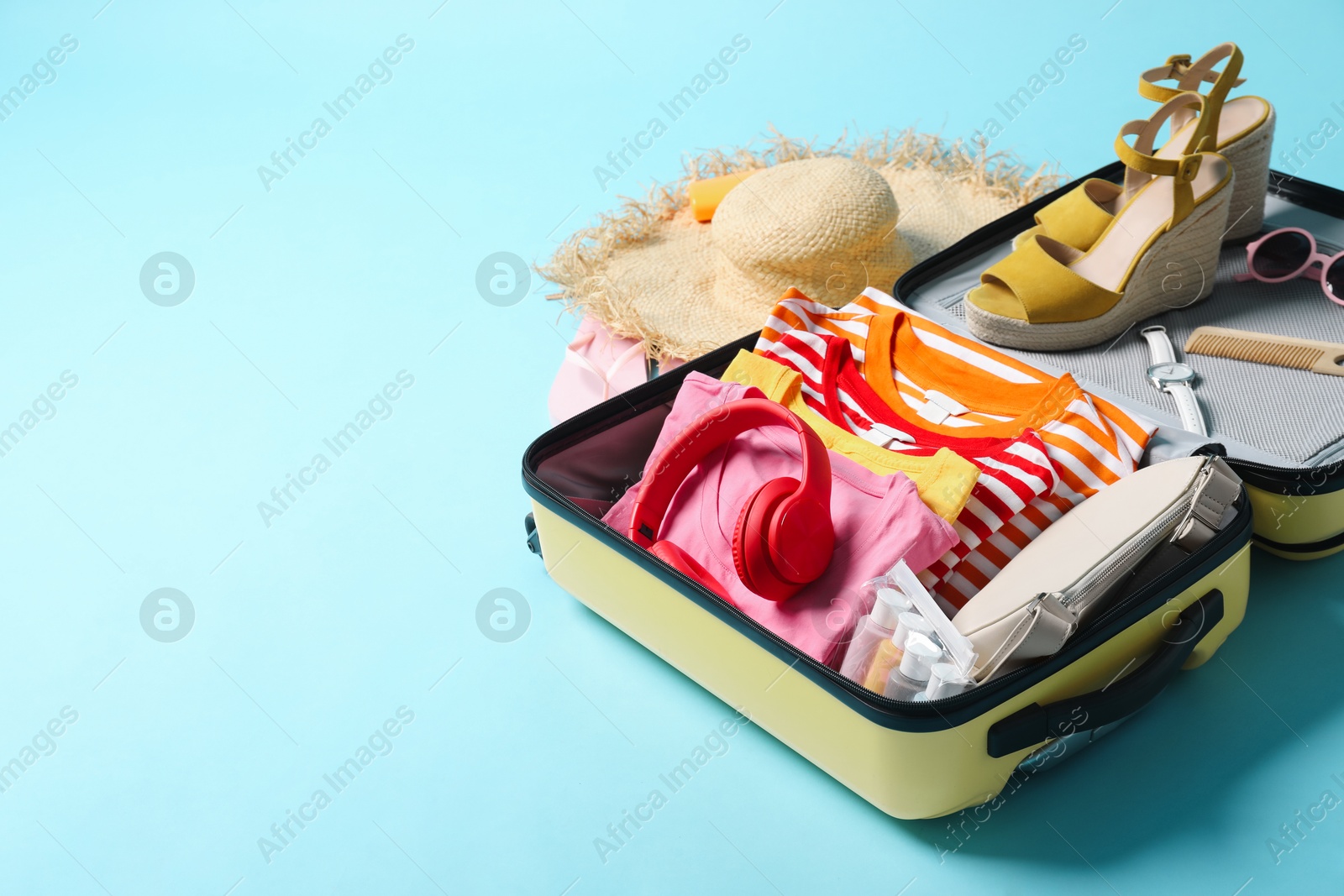 Photo of Open suitcase with traveler's belongings on light blue background, space for text