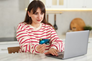 Photo of Online banking. Woman with credit card and laptop paying purchase at table indoors