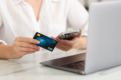 Photo of Online banking. Woman with credit card and laptop paying purchase at white marble table, closeup