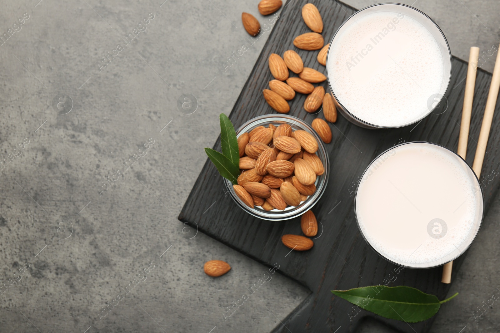 Photo of Glasses of almond milk and almonds on grey table, top view. Space for text