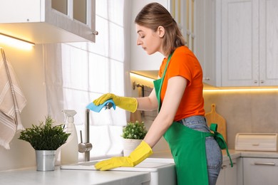 Photo of Professional janitor wearing uniform cleaning tap in kitchen