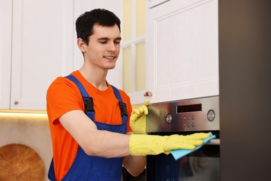 Photo of Professional janitor wearing uniform cleaning electric oven in kitchen