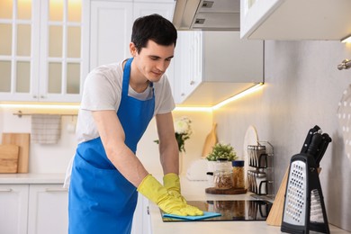 Photo of Professional janitor wearing uniform cleaning countertop in kitchen