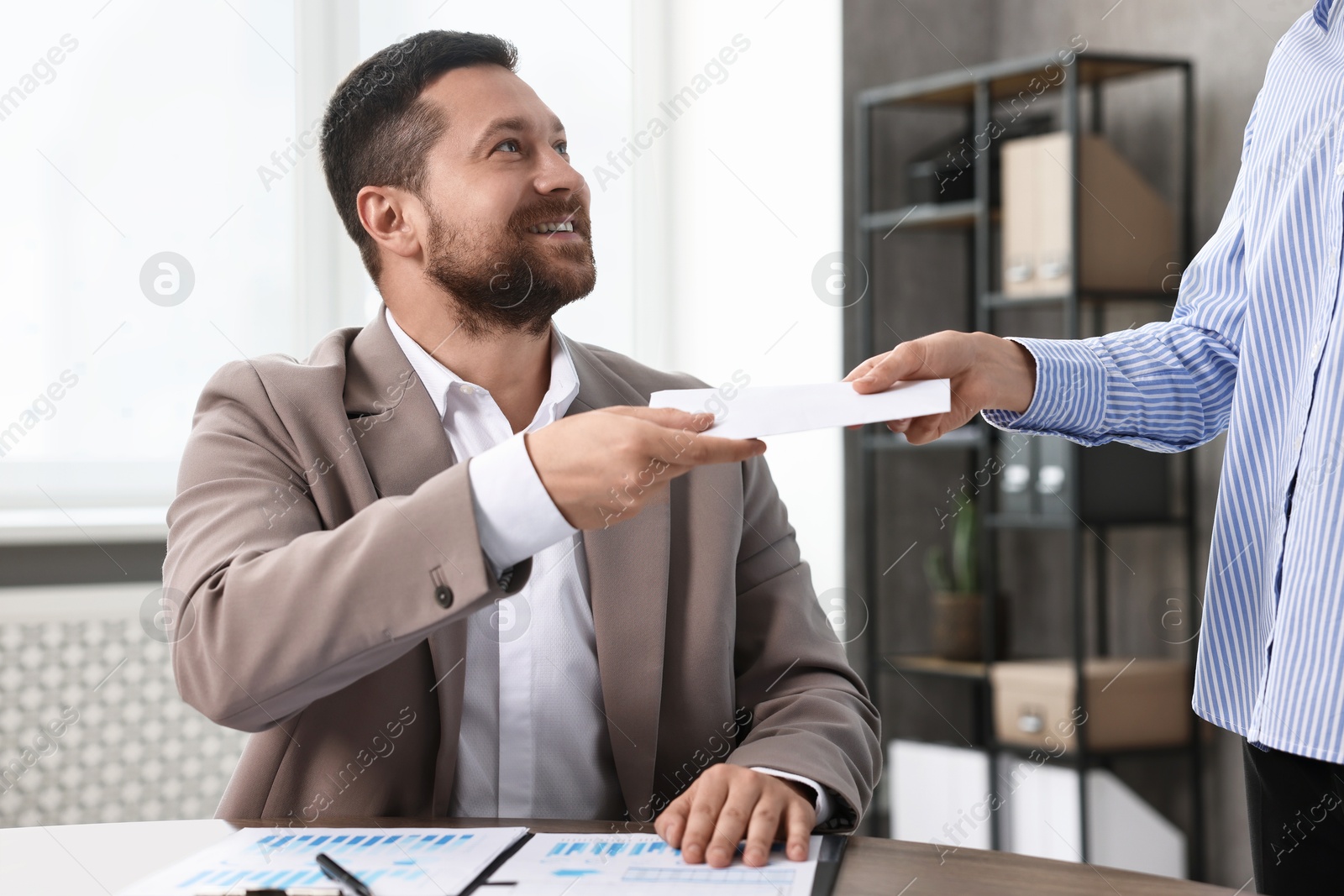 Photo of Boss giving salary in paper envelope to employee indoors