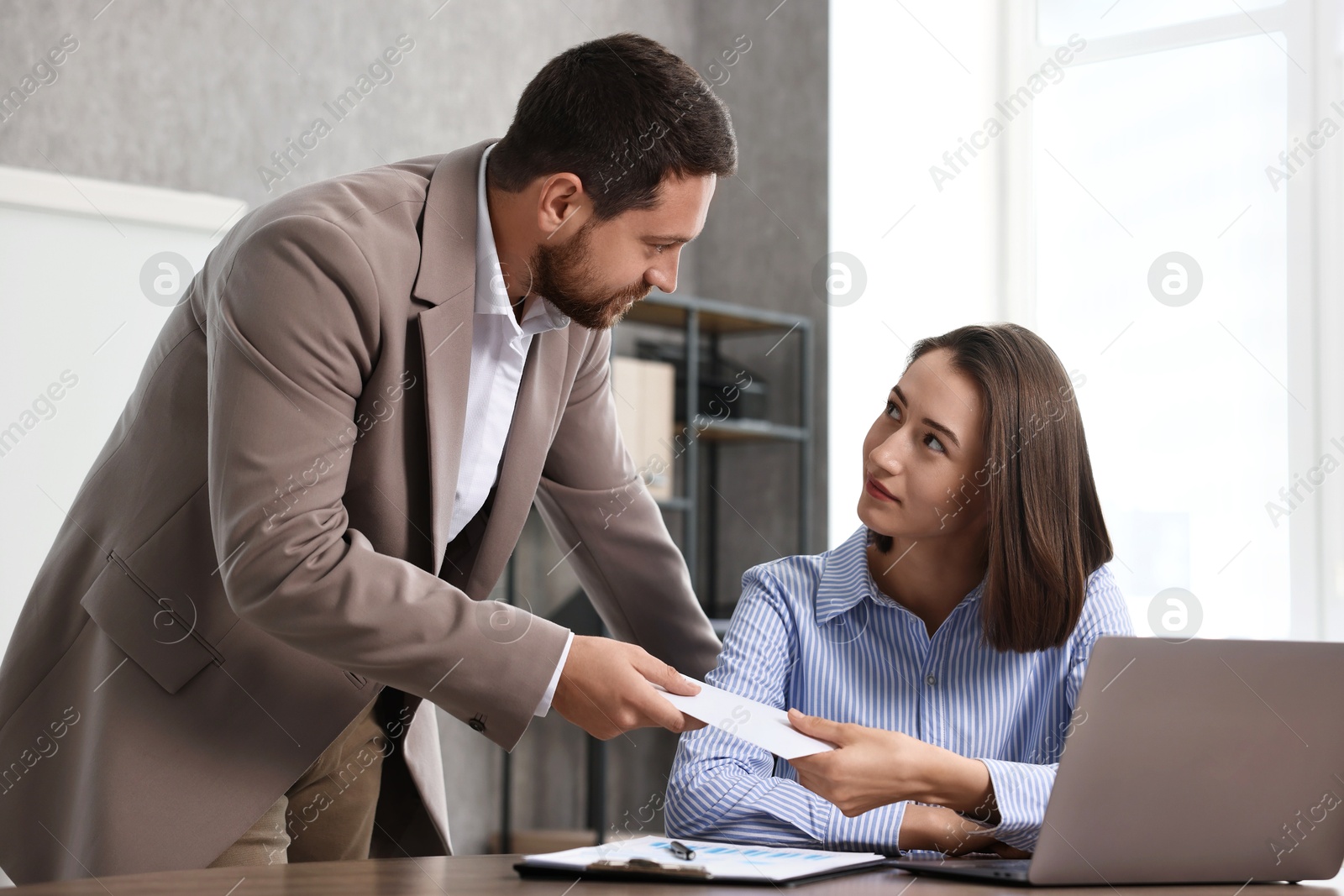 Photo of Boss giving salary in paper envelope to employee indoors