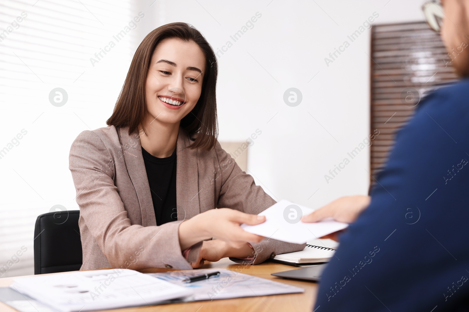 Photo of Boss giving salary in paper envelope to employee indoors