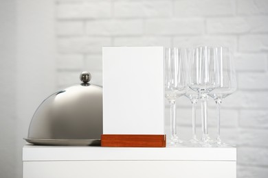 Photo of Menu holder, clean glasses and tray with cloche on white table indoors