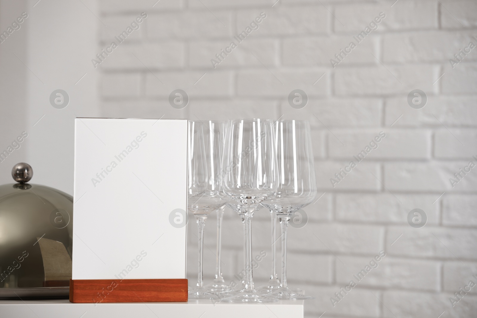 Photo of Menu holder, clean glasses and tray with cloche on white table indoors, space for text