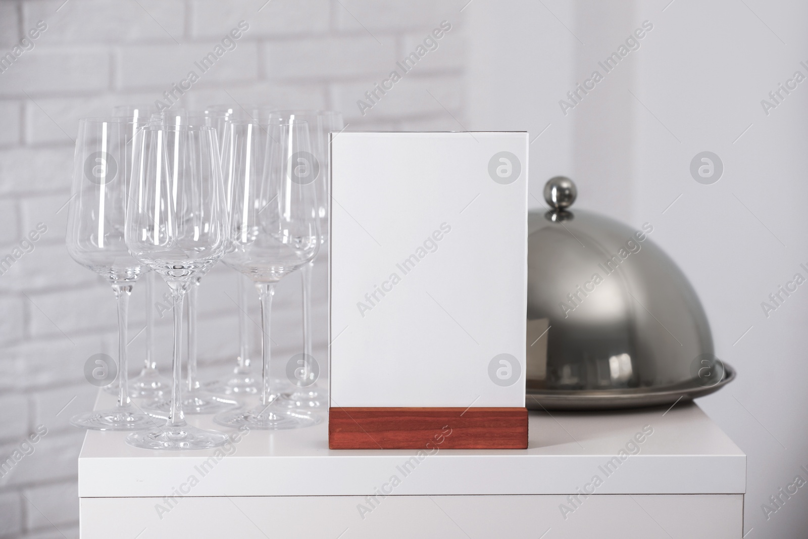 Photo of Menu holder, clean glasses and tray with cloche on white table indoors