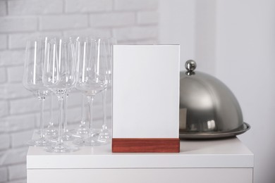 Photo of Menu holder, clean glasses and tray with cloche on white table indoors