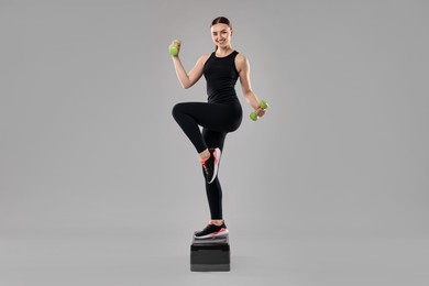 Photo of Young woman doing aerobic exercise with dumbbells and step platform on light background